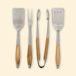 Set de quatre ustensiles de cuisson en inox avec manches en bois, comprenant deux spatules, une pince et une fourchette, présentés de face alignés verticalement.