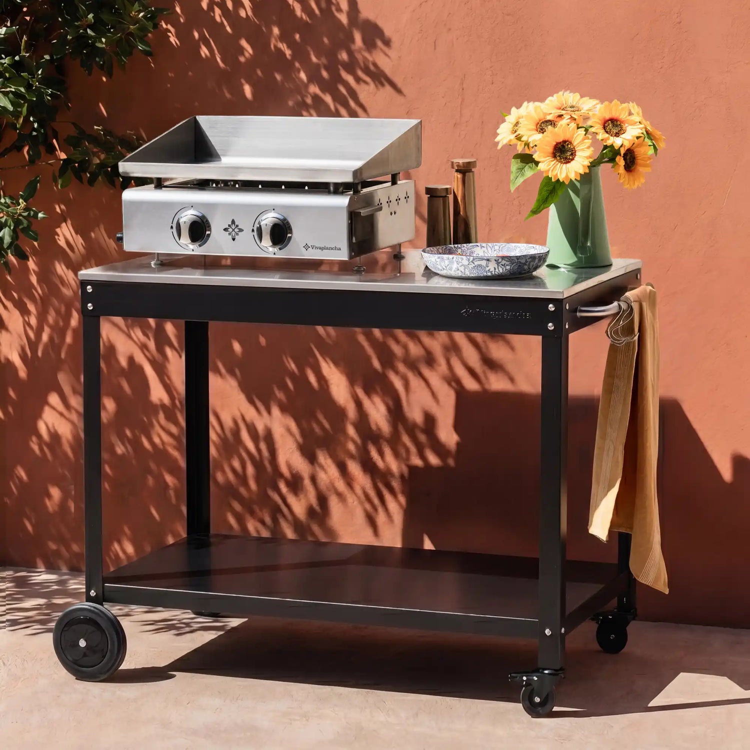 Plancha Vivaplancha installée sur la desserte Oliva, avec bouquet de tournesols et bol sur le plan de travail, en extérieur. ::visuel:sanscache