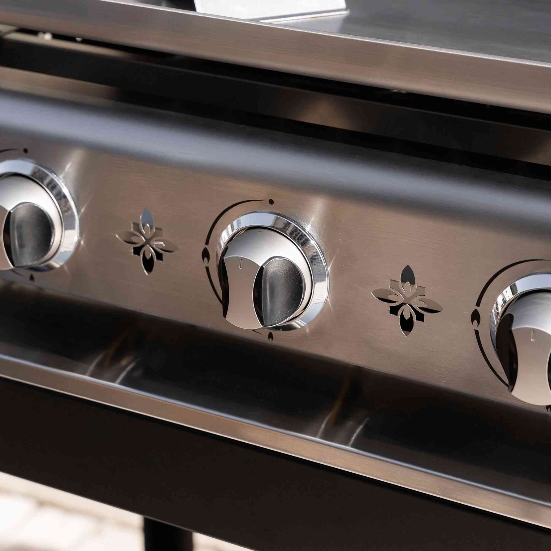 Gros plan sur les boutons de commande en inox d’une plancha gaz Vivaplancha, avec motifs décoratifs découpés dans la façade en acier inoxydable.