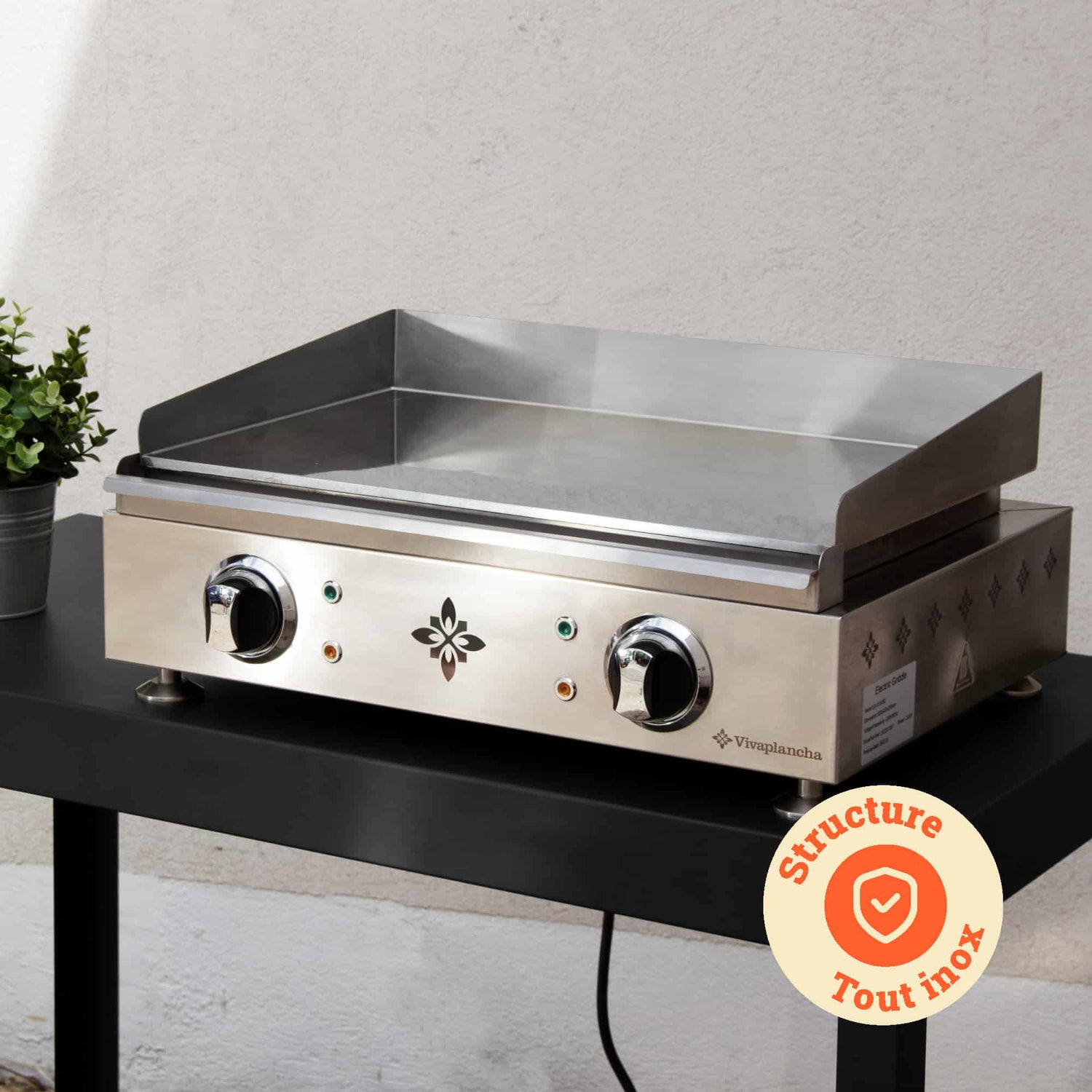 Plancha Vivaplancha appoggiata su un tavolo da esterno, con la sua struttura completamente in acciaio inox messa in risalto e un badge “Struttura tutta in inox” mostrato in un cerchio arancione.